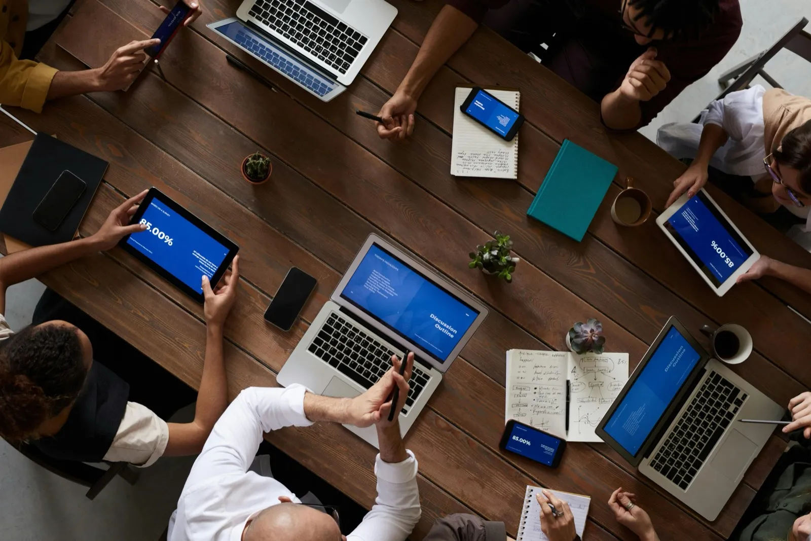 Overhead view of colleagues around a wooden table working on laptops, tablets and notebooks